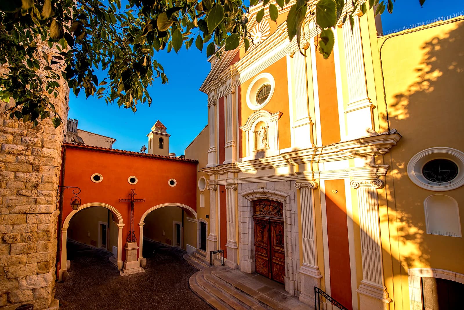 The striped ochre façade of Antibes Cathedral, Notre-Dame de la Platea, and its courtyard cross