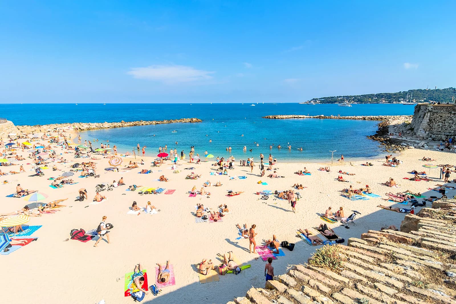 Families on the sand of the Gravette beach beneath the walls of Old Antibes in summer